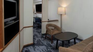 A hotel room with a flat-screen TV, a sofa, a small table, a lamp, and a desk with a chair.