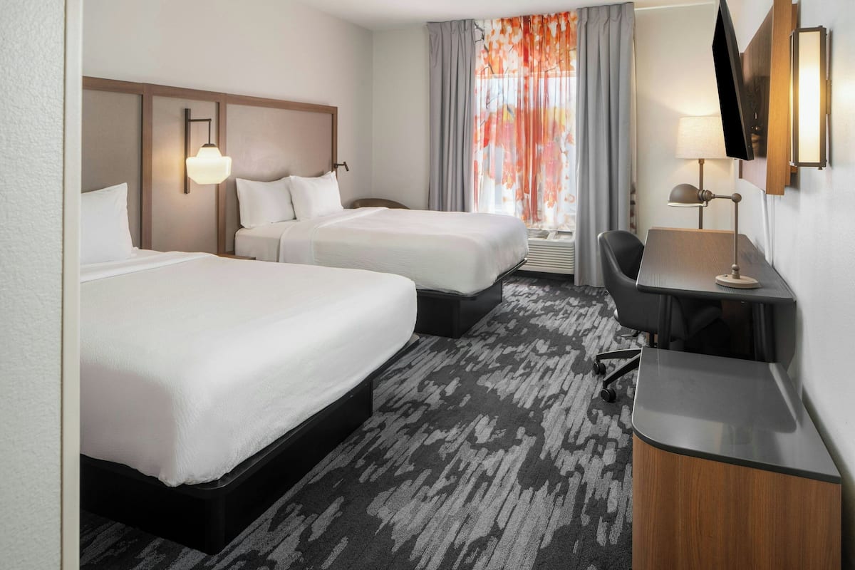 A hotel room with two beds, a desk, a chair, a TV, and a window with curtains.