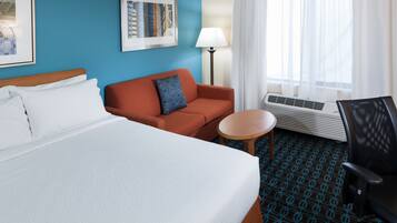 Habitación de hotel con una cama grande, un sofá, una mesita, una silla, equipo de aire acondicionado y una ventana con cortinas.