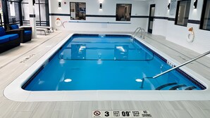 A modern indoor swimming pool with clear water, a lifeguard chair, and a pool rule sign indicating a depth of 3 feet and 9 inches.