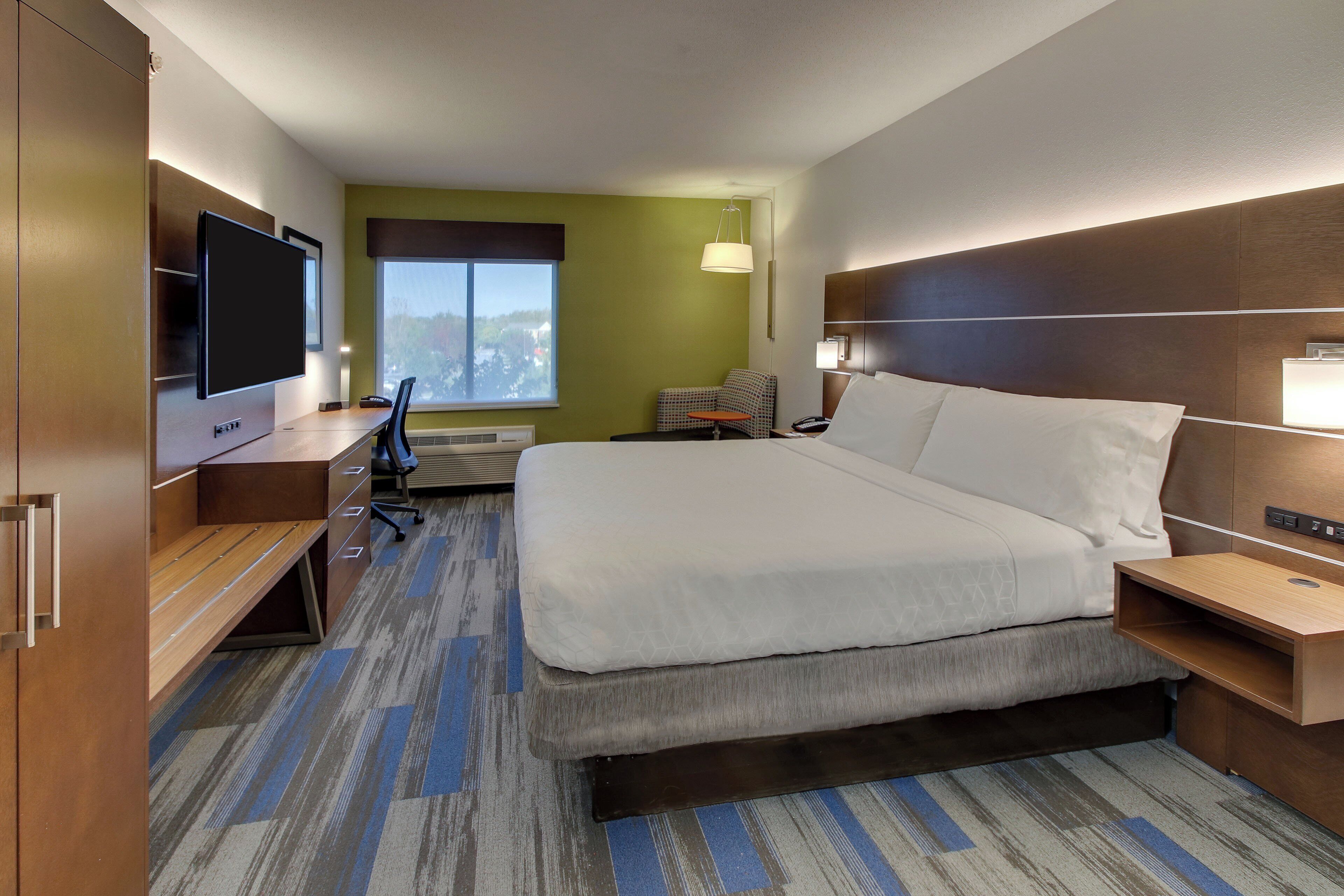 Habitación de hotel con cama, escritorio, silla, televisor y vista a la ciudad.
