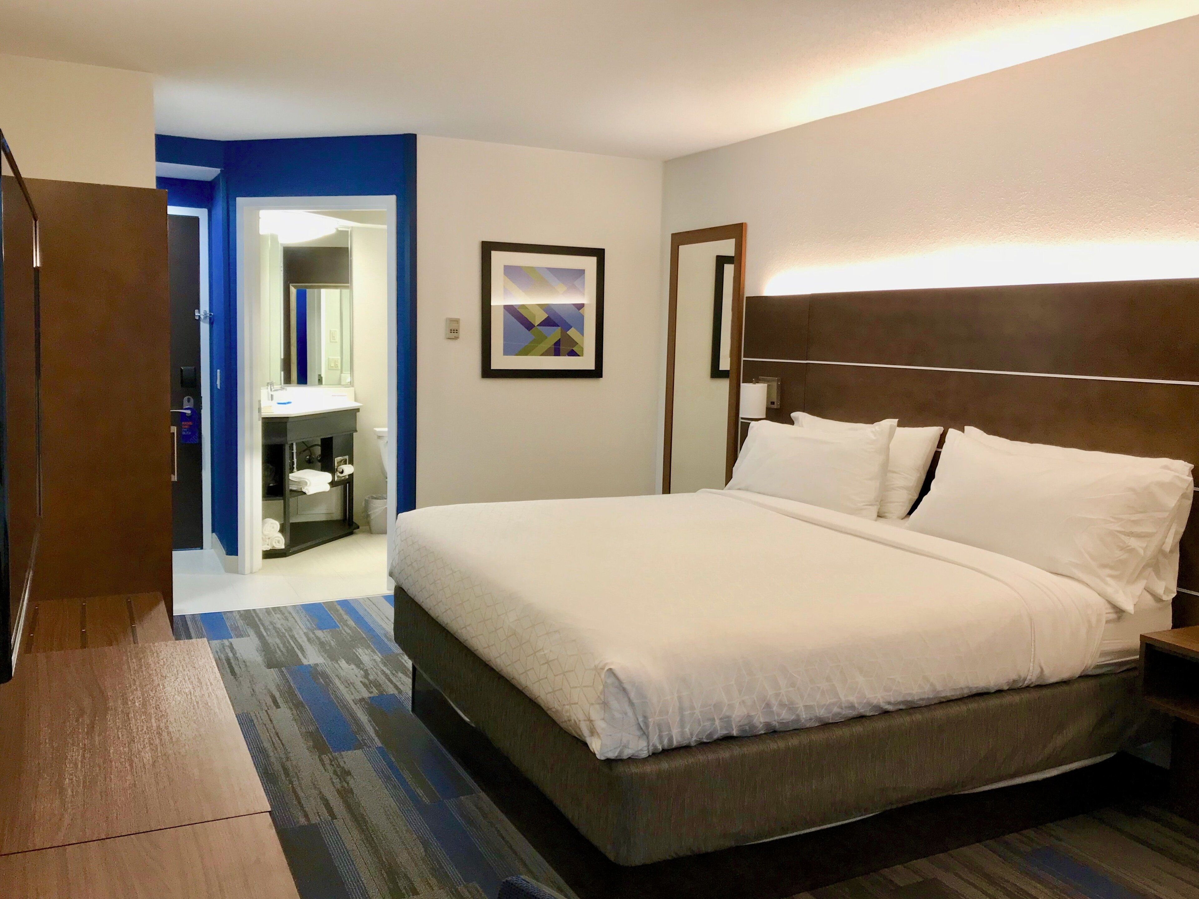 A hotel room with a large bed, a bathroom with a mirror, and a door leading to another room.
