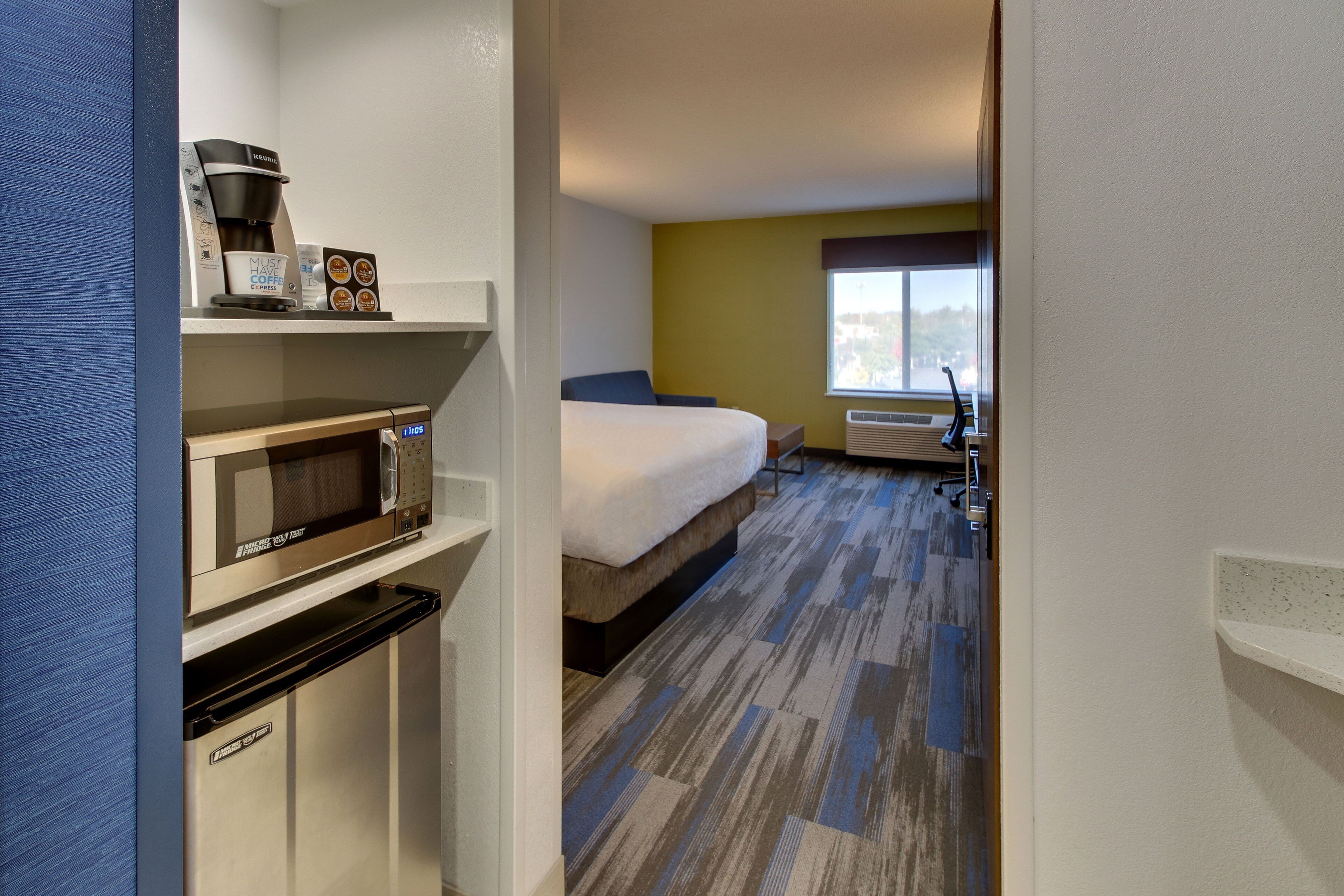 Una habitación de hotel con cama, microondas, cafetera y una kitchenette pequeña.