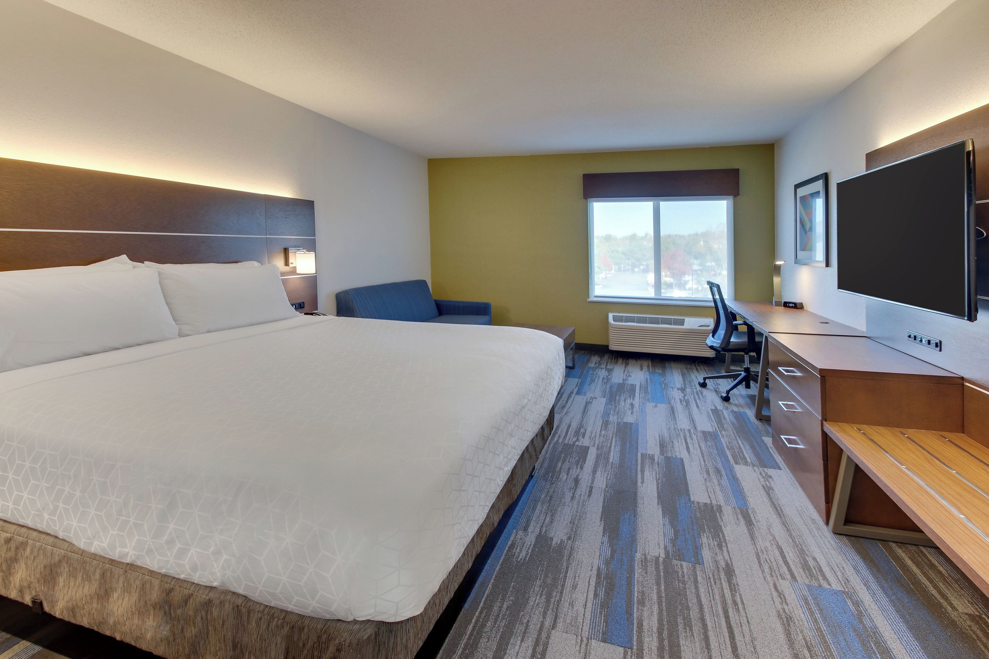A hotel room with a large bed, a desk, a chair, a TV, and a window.