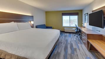 A hotel room with a large bed, a desk, a chair, a TV, and a window.