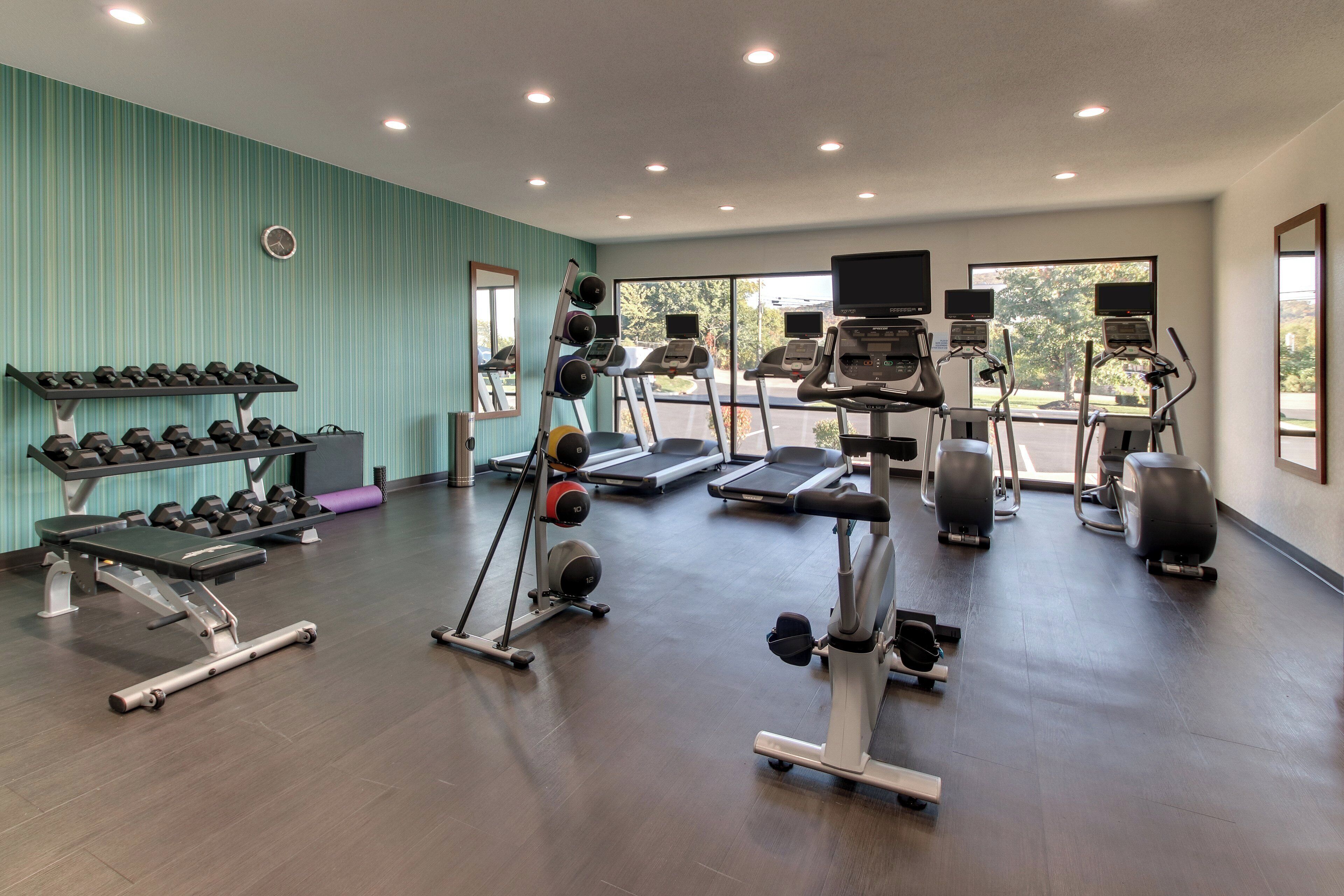 Un gimnasio con cintas de correr, elípticas, prensa de banca y pesas sueltas.