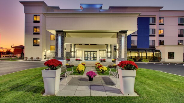 A modern hotel entrance with a covered walkway, potted plants, and a well-maintained lawn. - Holiday Inn Express Fishkill-Mid Hudson Valley by IHG (Fishkill)