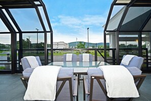 A glass-top table with six chairs, each with a white towel, in a modern outdoor setting with a view of a road and buildings.