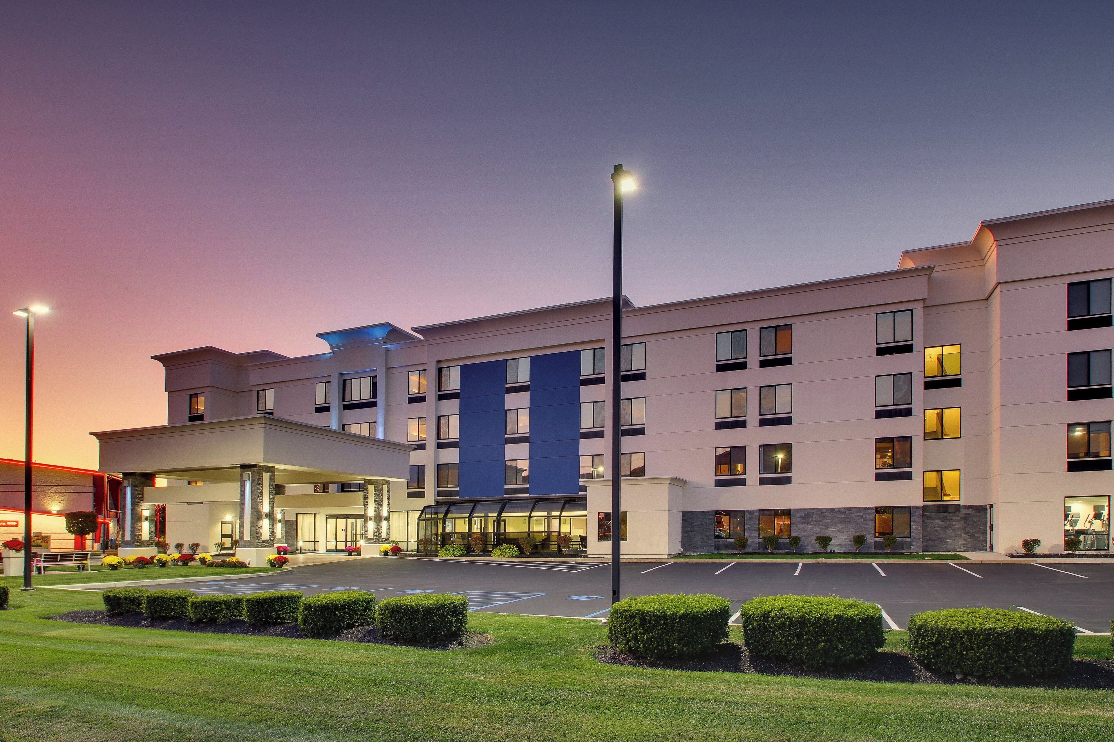 A multi-story hotel with a central entrance, a parking lot, and well-maintained landscaping.