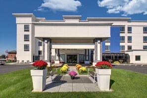 A modern hotel entrance with a covered walkway, potted plants, and a clear sky.