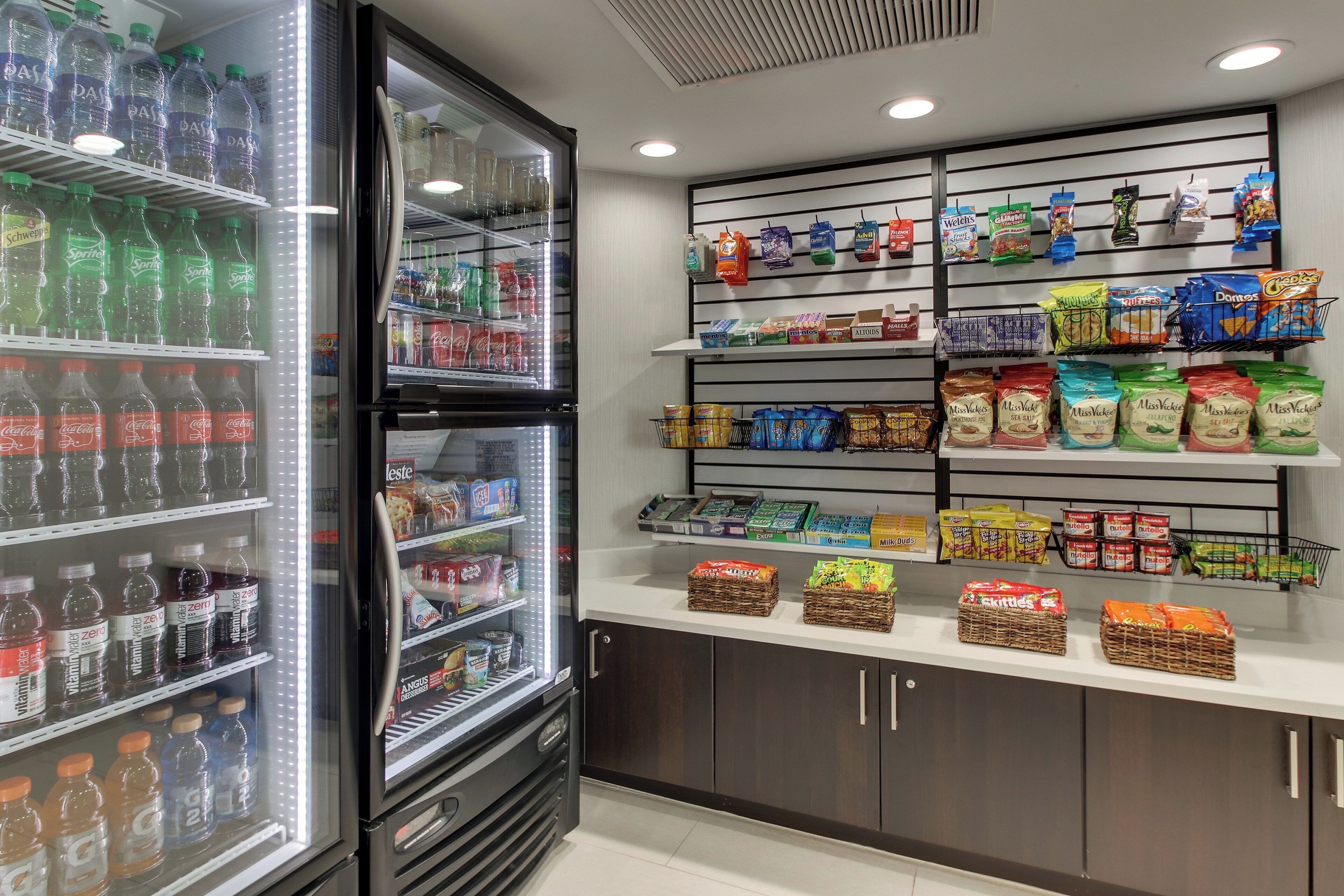 Mostrador refrigerado con bebidas variadas y estante lleno de papas fritas y otros bocadillos.
