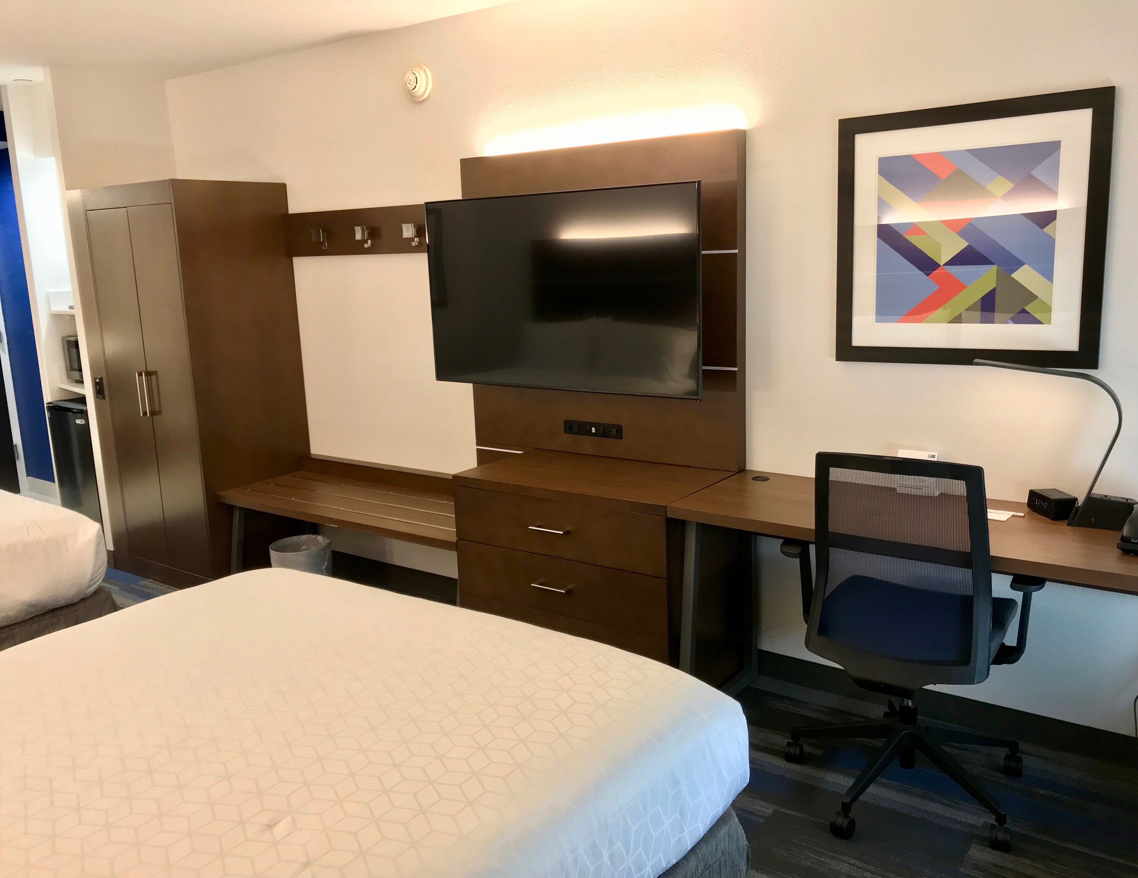 A hotel room with a bed, a desk with a computer, a TV, a chair, and a wardrobe.