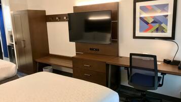 A hotel room with a bed, a desk with a computer, a TV, a chair, and a wardrobe.