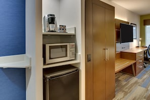 Una kitchenette compacta con microondas, cafetera y refrigerador.