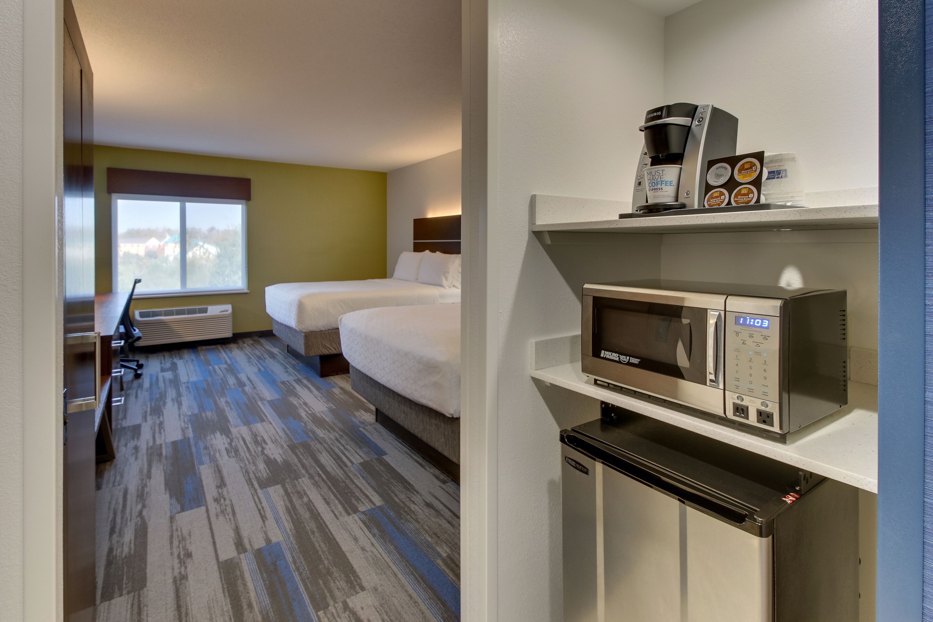 A hotel room with two beds, a microwave, a coffee maker, and a mini fridge.