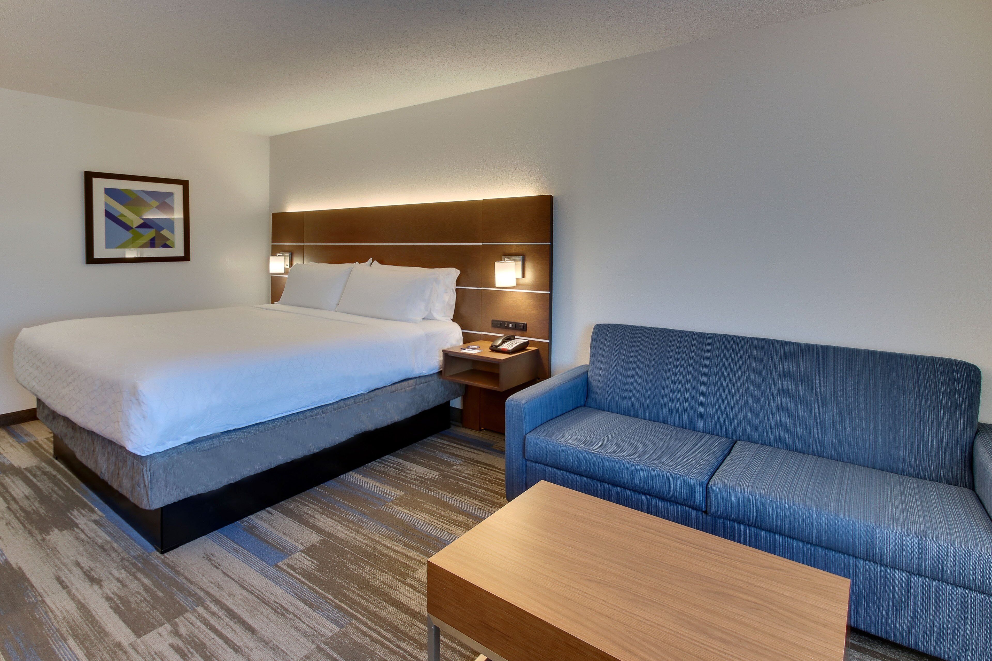 Een hotelkamer met een bed, een blauwe bank, een houten bijzettafeltje en een nachtkastje met een lamp.