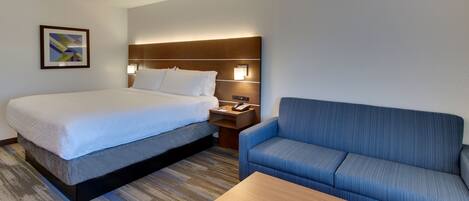 Een hotelkamer met een bed, een blauwe bank, een houten bijzettafeltje en een nachtkastje met een lamp.