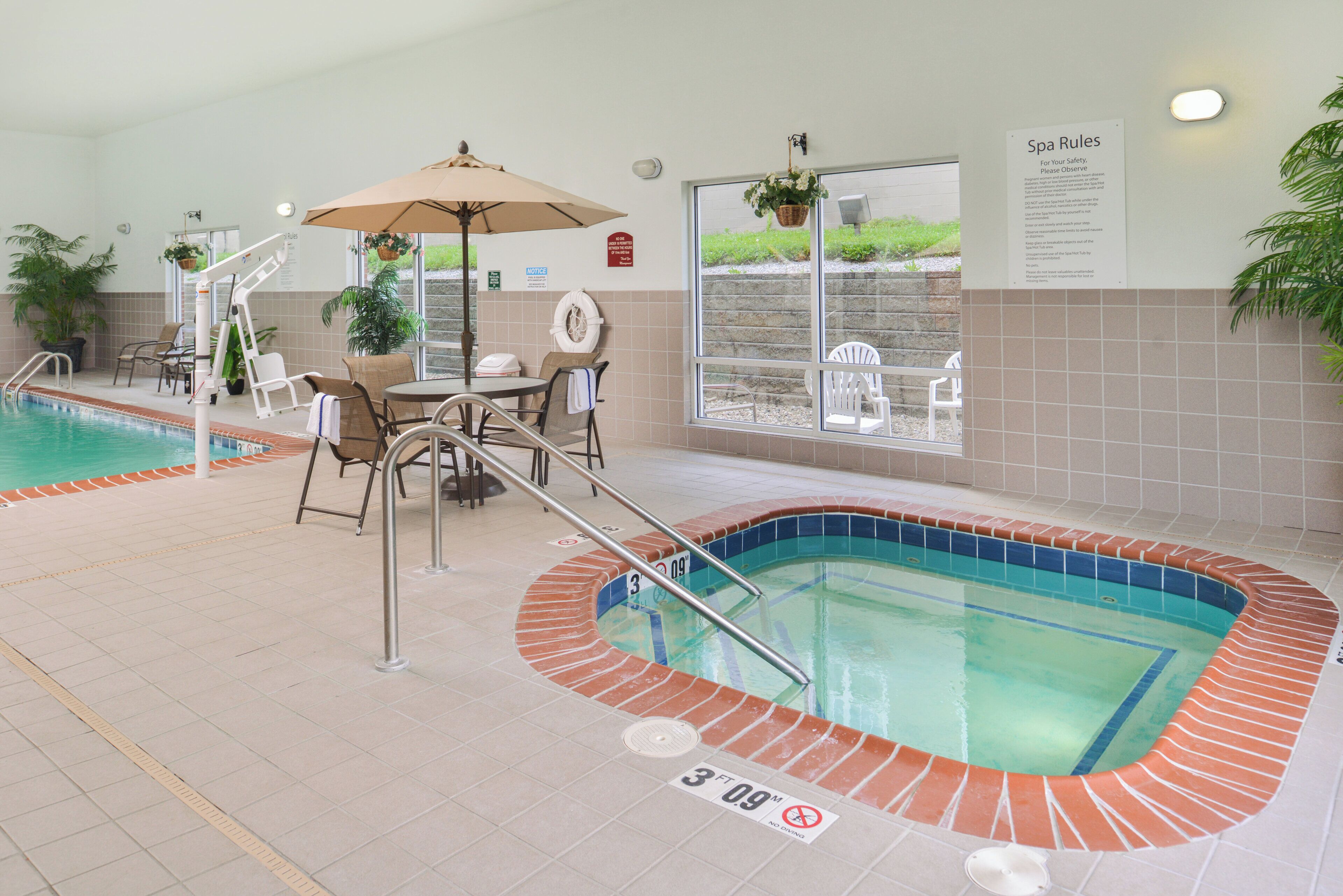 An indoor swimming pool area with a hot tub, lounge chairs, and a table.