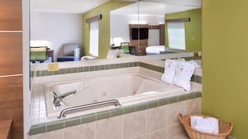 A bathroom with a large bathtub, a mirror, a green wall, a wicker basket with towels, and a chair.