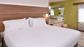 Una cama grande con ropa de cama blanca, un cabecero de madera, una mesita de noche y un espejo encima.