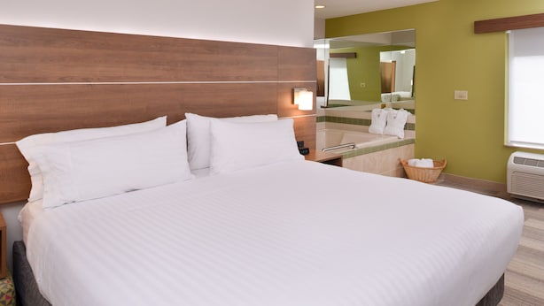 Una cama grande con ropa de cama blanca, un cabecero de madera, una mesita de noche y un espejo encima.