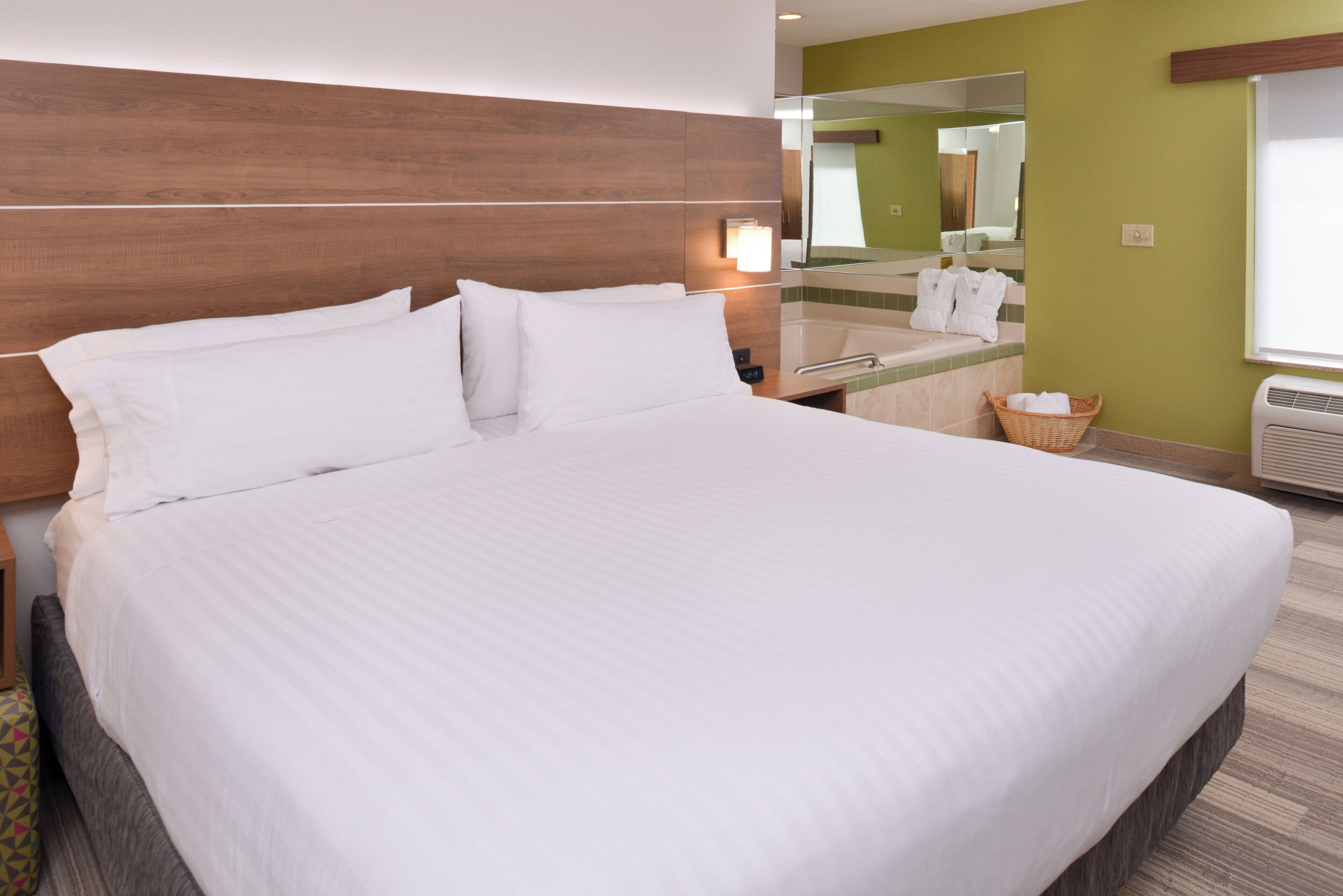 Una habitación de hotel con una cama grande, una mesita de noche, un espejo, una ventana y aire acondicionado instalado en la pared.