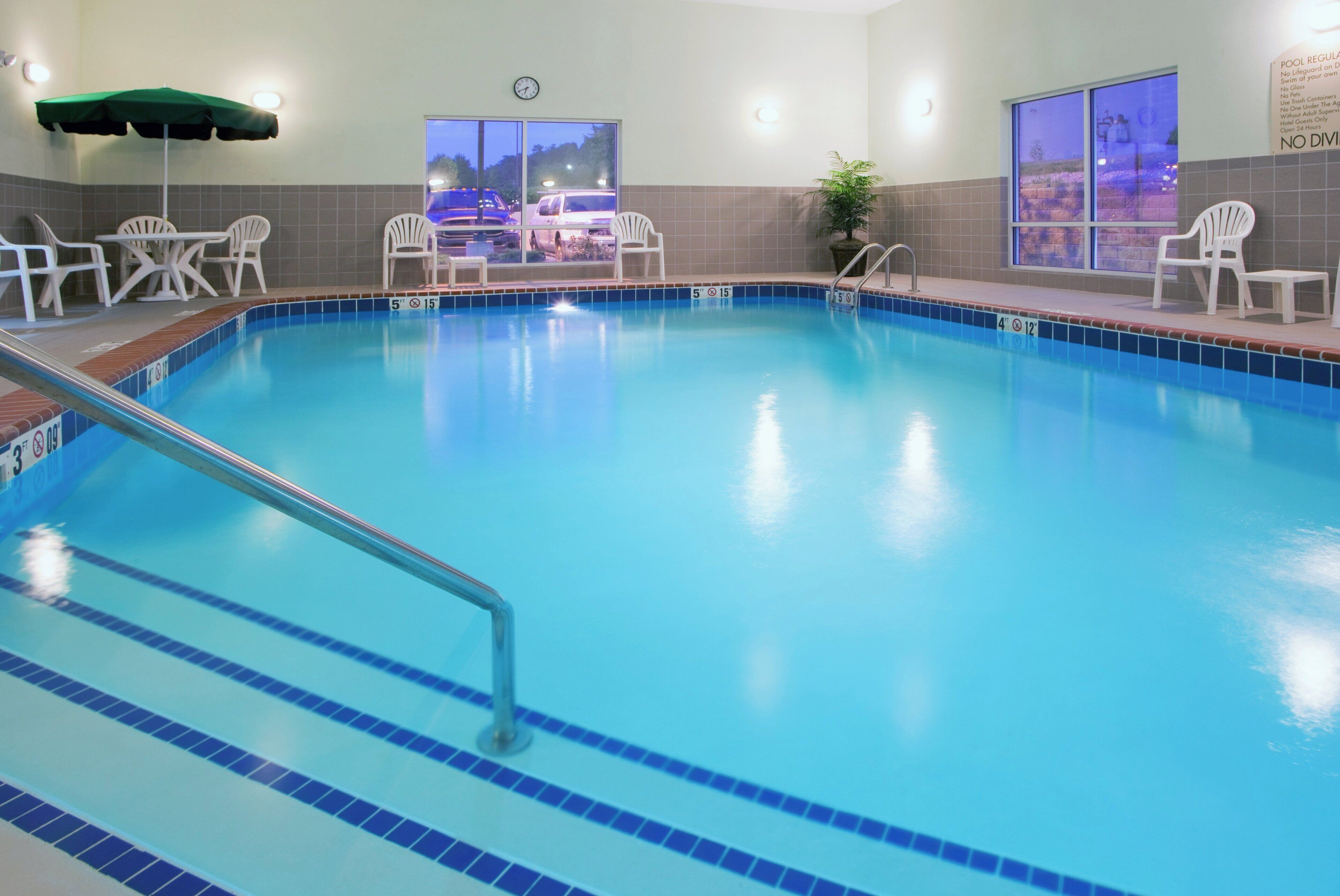 An indoor swimming pool with clear lane markings, a lifeguard chair, and a view of the outside through large windows.