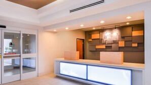 Un área de recepción de diseño moderno, con puerta de vidrio, mostrador de recepción con paneles iluminados y una lámpara fijada a la pared.