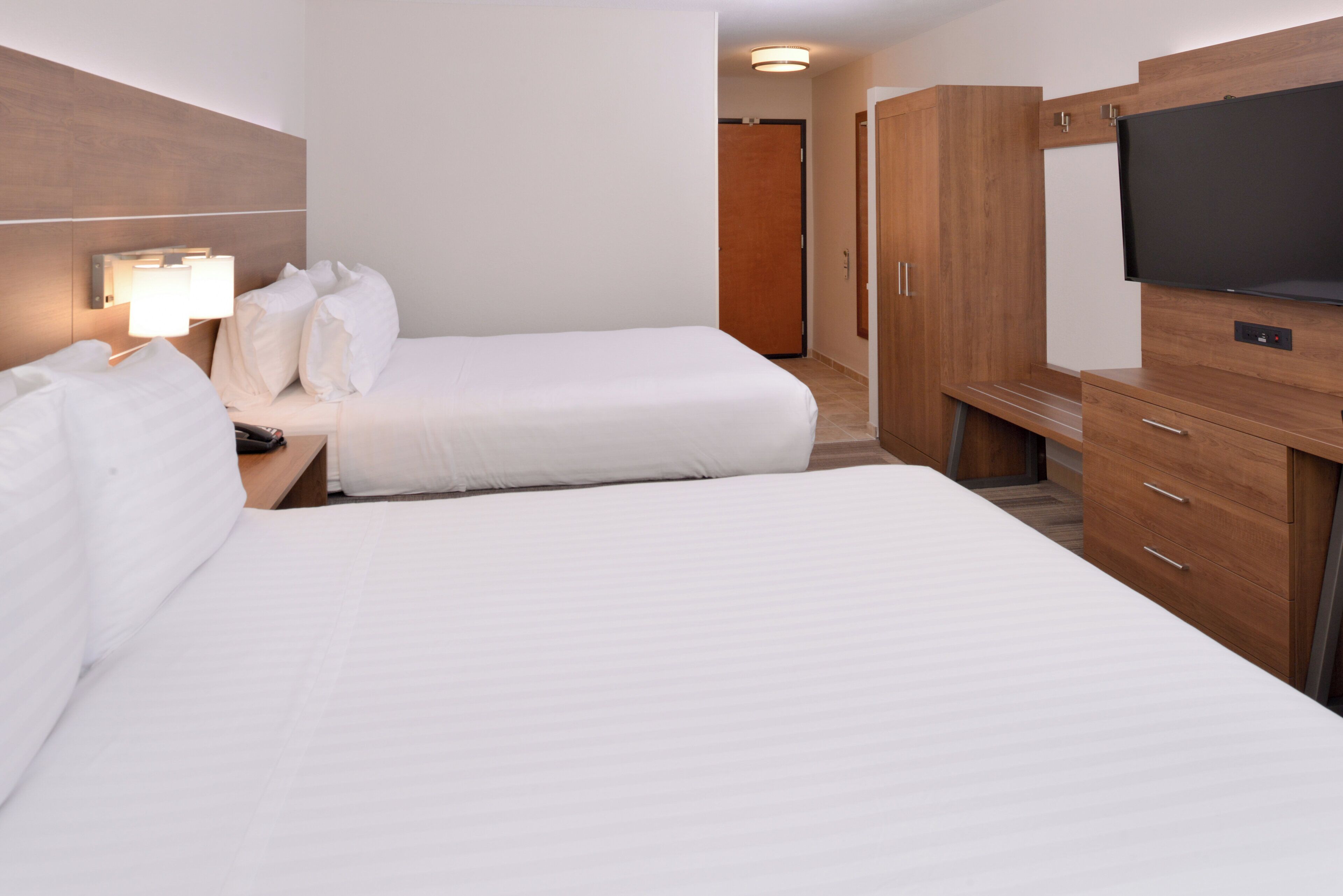 Una habitació d'hotel amb dos llits, una televisió, una taula de nit amb làmpada i un armari.