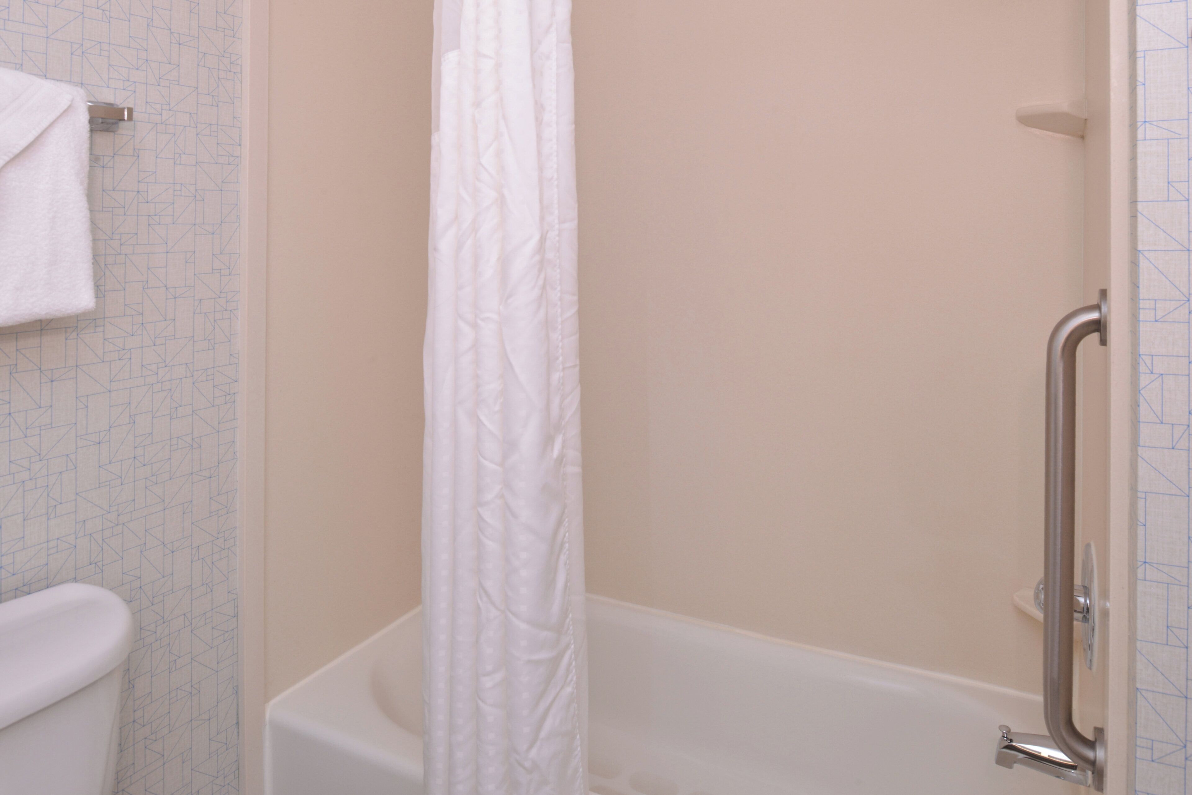 A bathroom with a bathtub, a shower curtain, and a handrail.