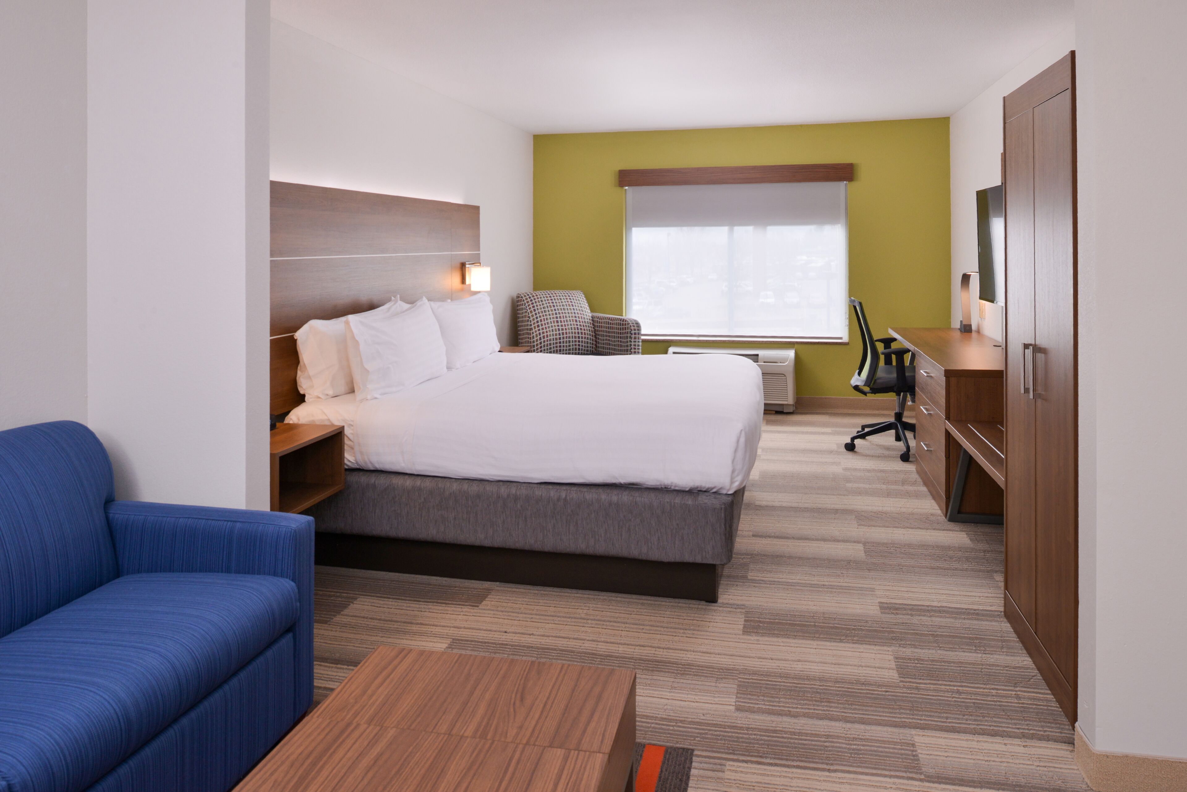 A hotel room with a bed, a blue sofa, a wooden coffee table, a desk with a chair, and a wardrobe.