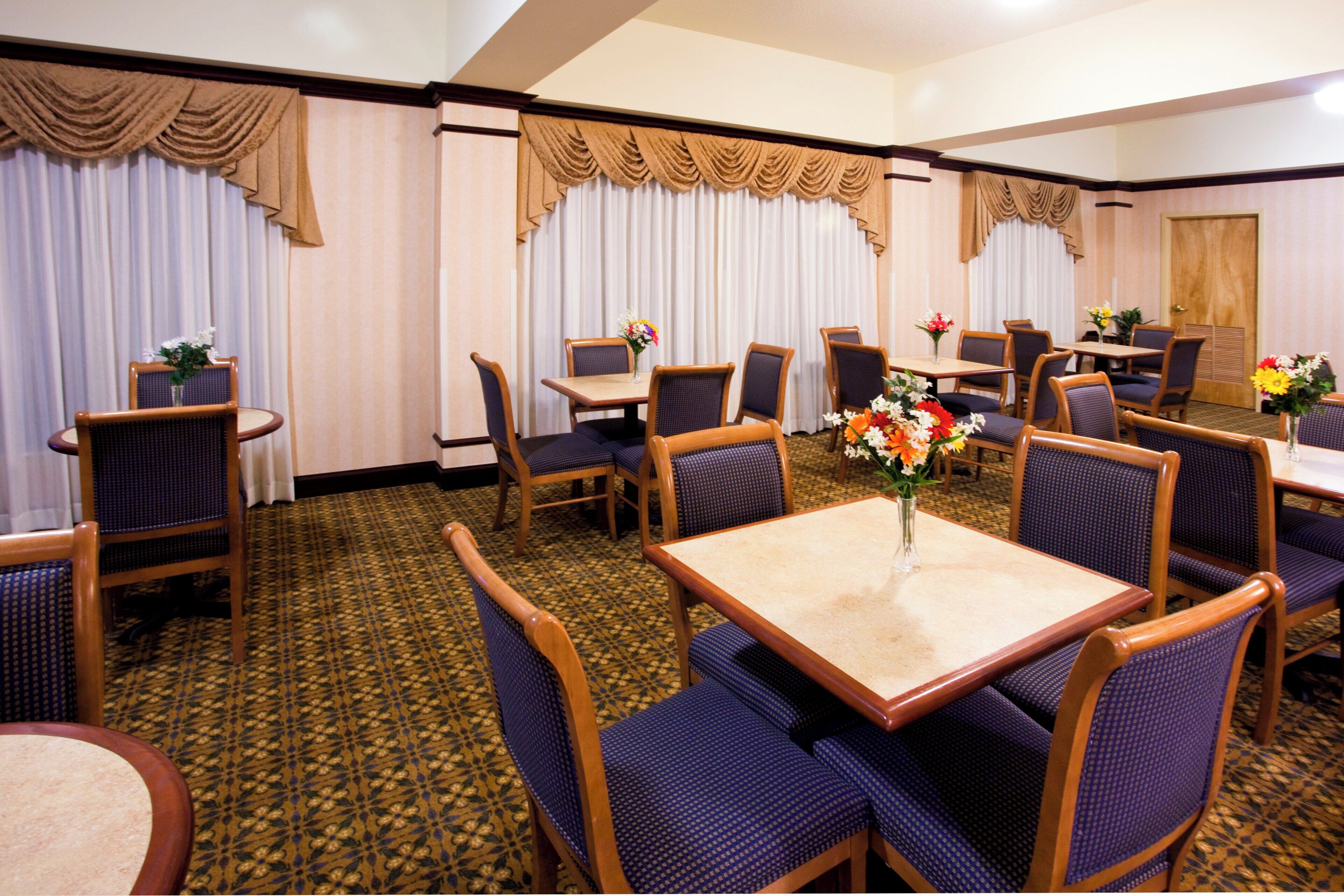 Une salle à manger d’hôtel avec plusieurs tables et chaises, dont certaines sont ornées de centres de table floraux.