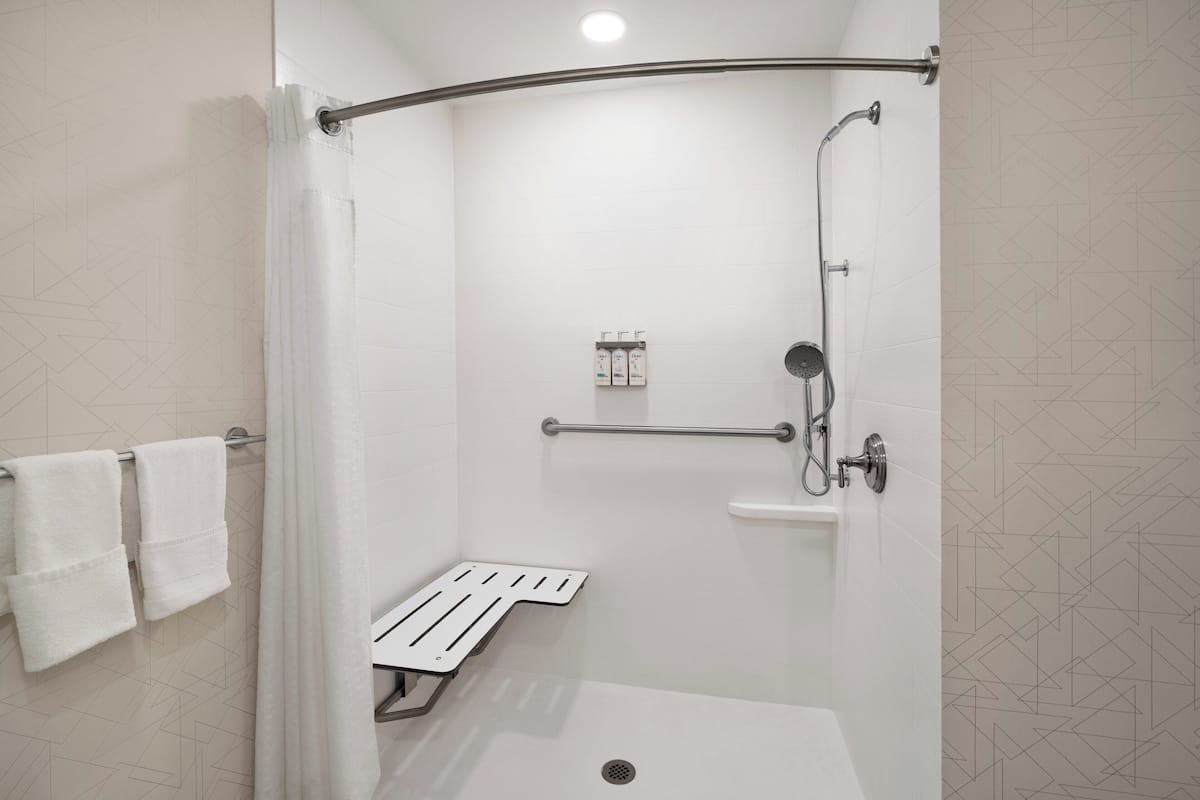 A modern shower area with a glass door, a handheld showerhead, a handheld shower attachment, and a small shelf with toiletries.