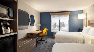 A hotel room with a bed, a desk with a chair, a microwave, a coffee maker, and a window with a view of trees.