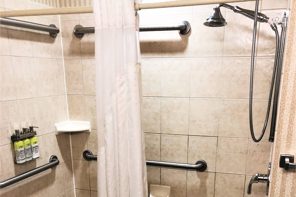 A shower area with a grab bar, a handheld showerhead, and a white curtain.
