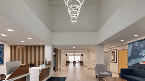 Un hall d'hôtel moderne avec un comptoir d'accueil, un espace salon et, au fond, une salle à manger.