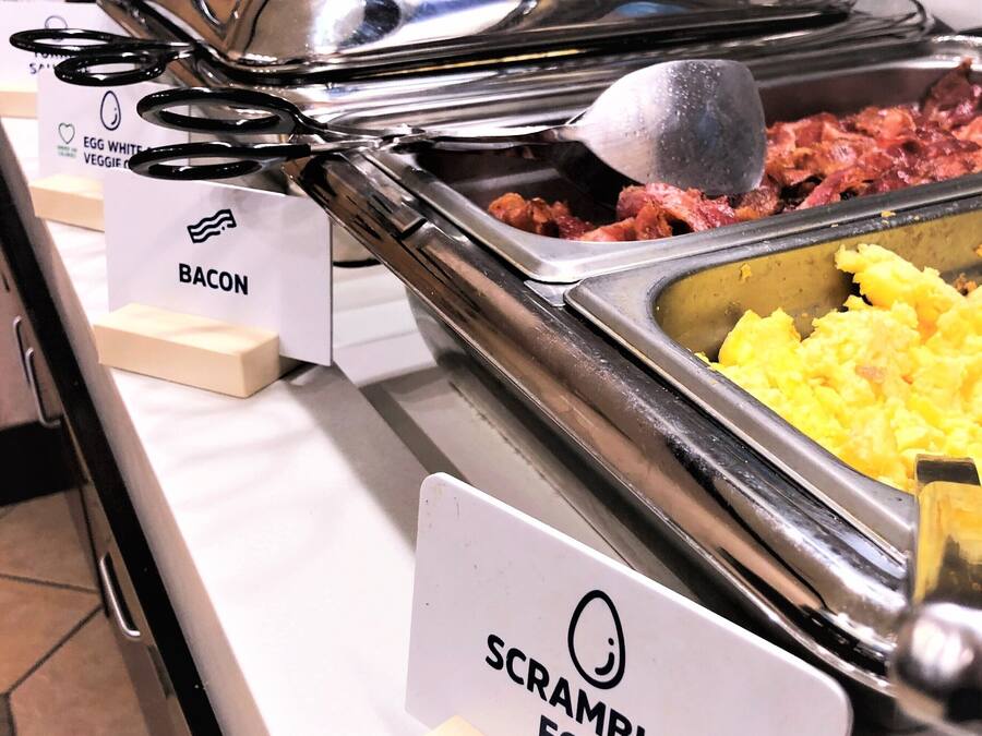 A buffet with labeled sections for scrambled eggs, bacon, and other dishes.
