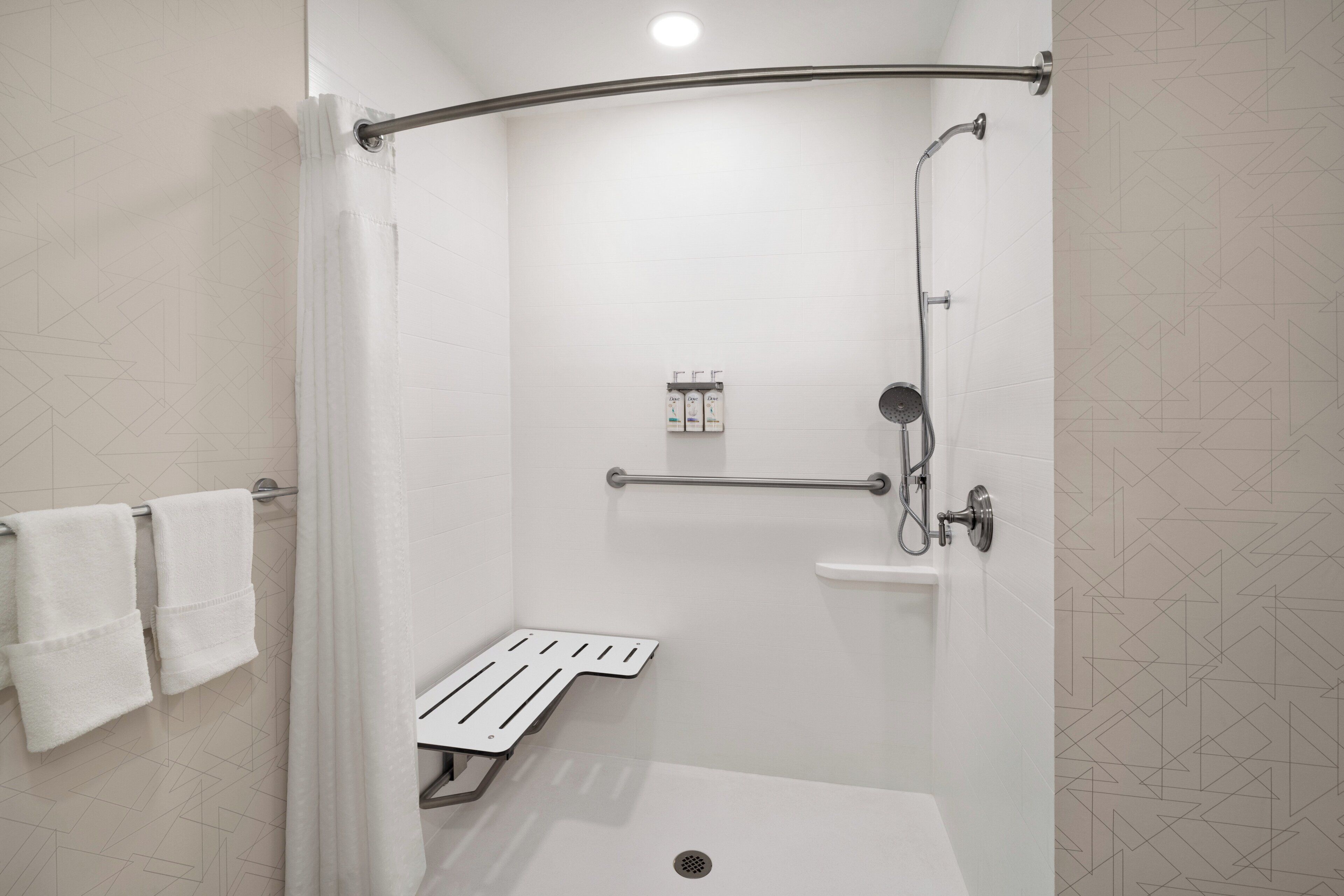 Un área de ducha moderna con puerta de vidrio, un cabezal de ducha manual y un accesorio de ducha manual, además de un estante pequeño con artículos de aseo.
