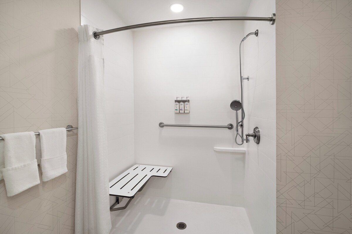 A modern shower area with a glass door, a handheld showerhead, a handheld shower attachment, and a small shelf with toiletries.