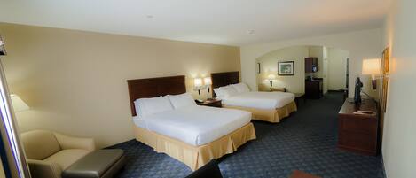 A hotel room with two beds, a desk, a chair, and a desk lamp.