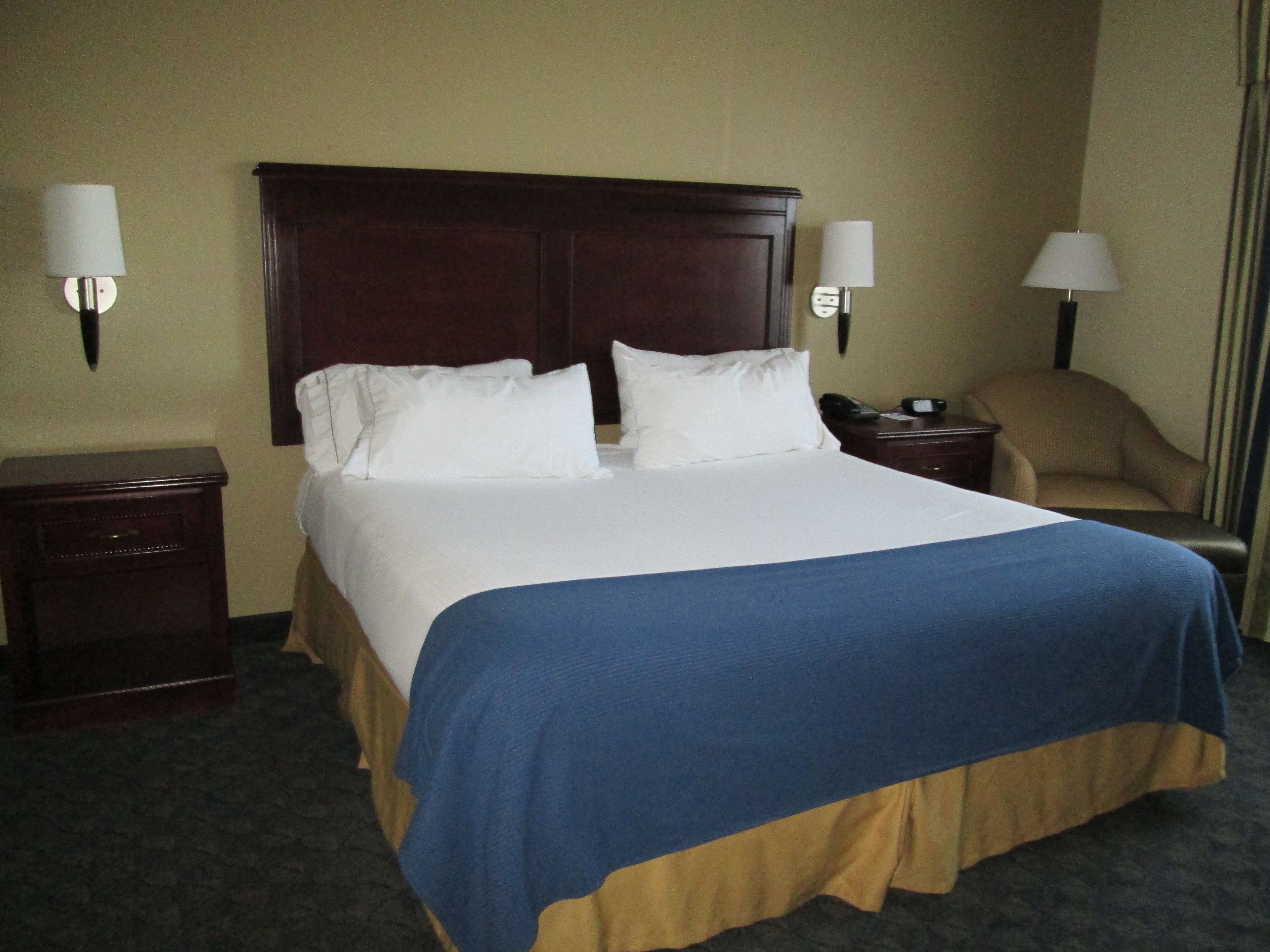 Une chambre d’hôtel avec un grand lit, deux tables de chevet, une chaise et deux lampes fixées au mur.