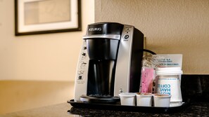 Une machine à café Keurig avec un bac d’égouttement, une dosette de café et une tasse de café posée sur un comptoir.