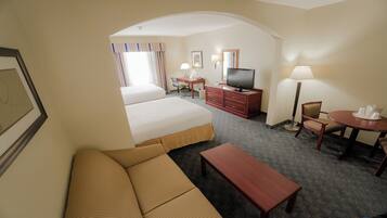Quarto de hotel com sofá, mesa pequena, televisão, escrivaninha e cadeira.