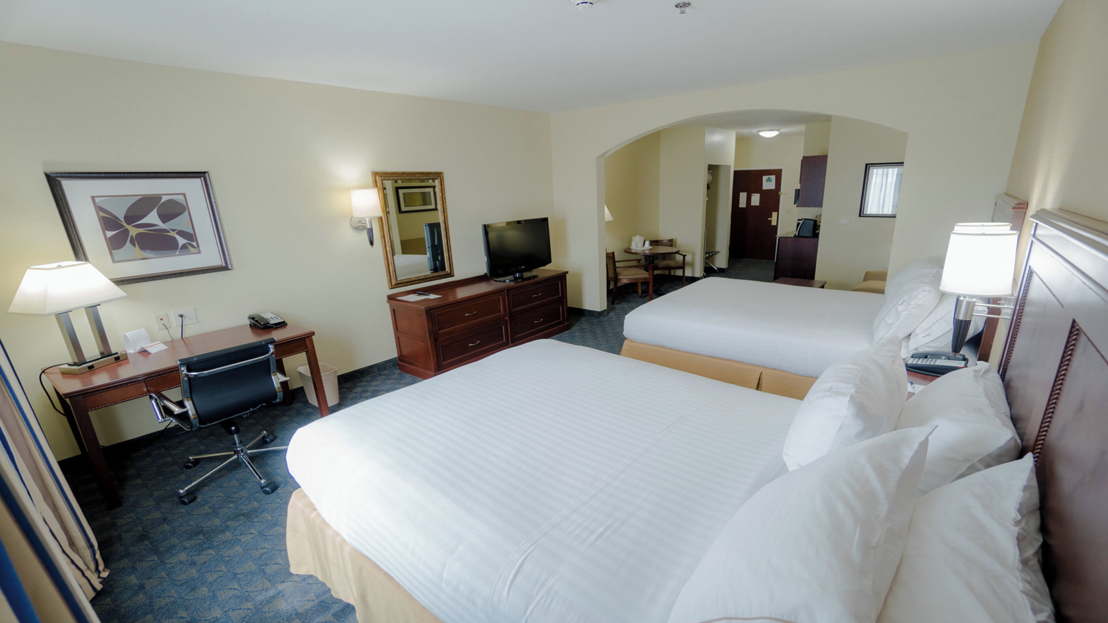 Habitación de hotel con dos camas, un escritorio con silla, televisor y baño visible a través de un arco.