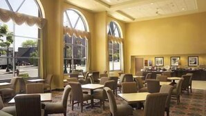 A hotel dining area with large windows, tables, and chairs.