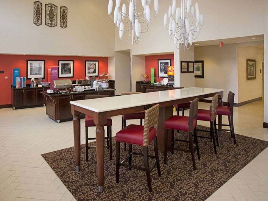 Un comedor de hotel con una larga mesa, sillas tapizadas en rojo, una alfombra estampada y un candelabro.