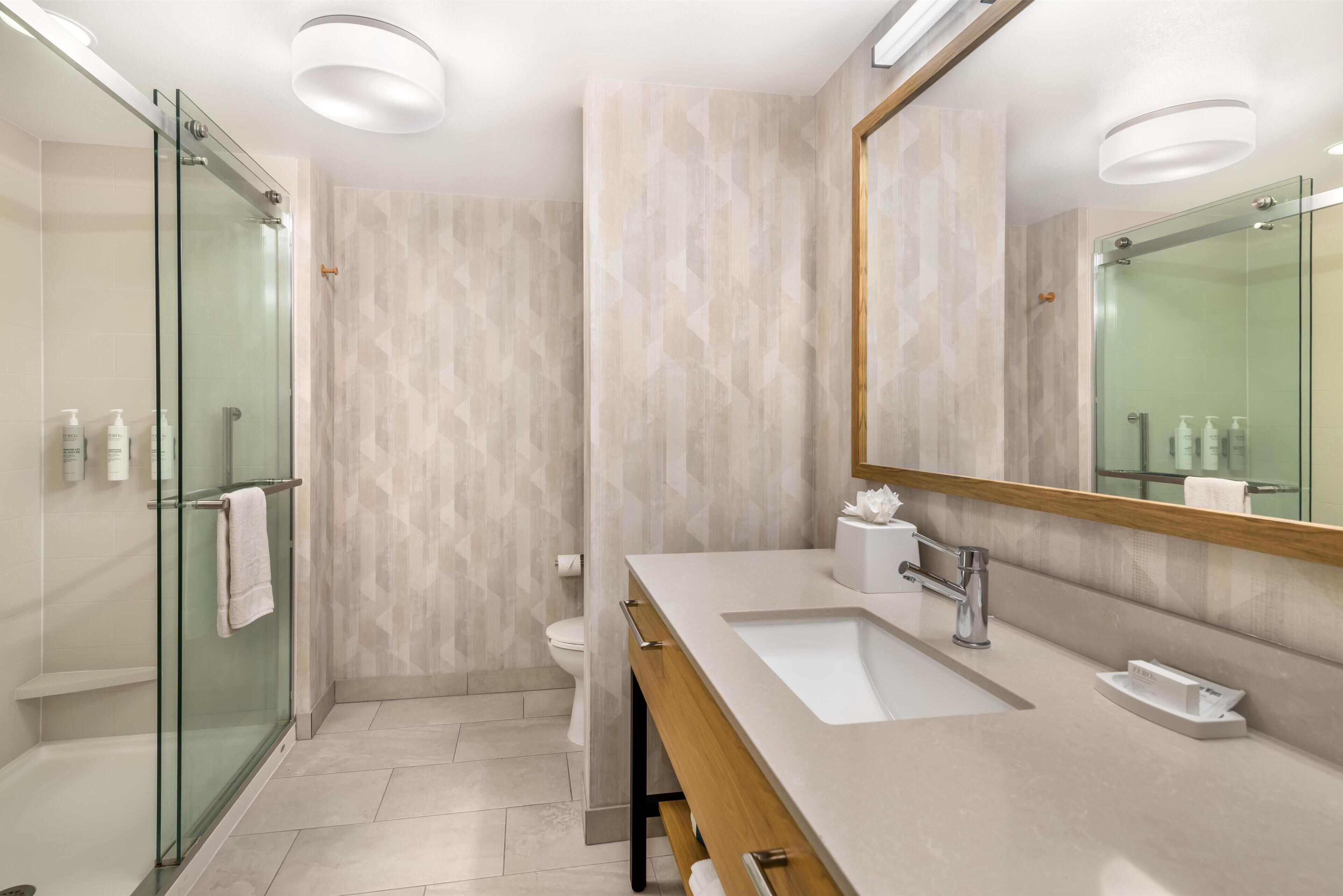 Un bagno moderno con cabina doccia in vetro, lavabo bianco e un grande specchio.