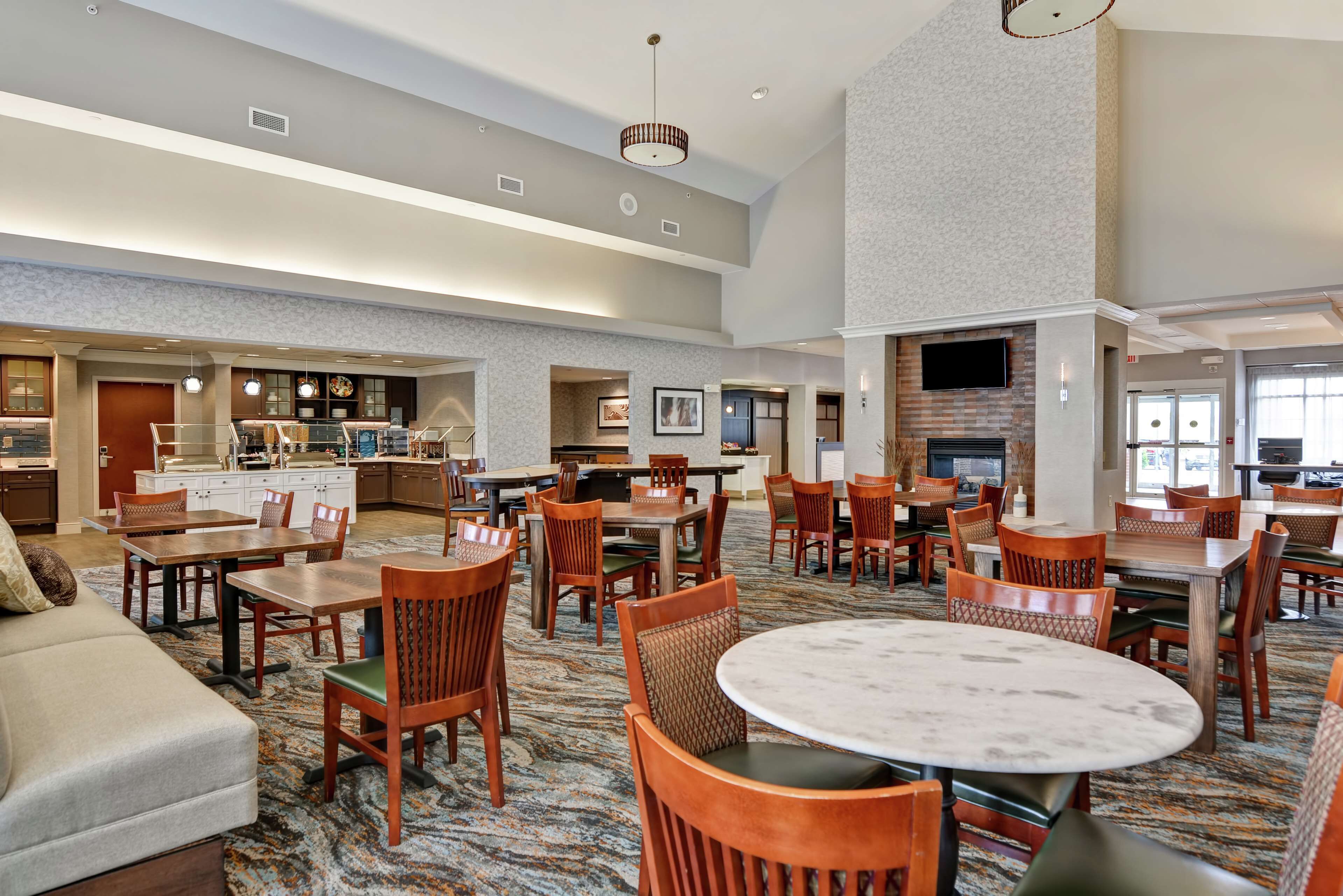 A spacious hotel lobby with multiple seating areas, a fireplace, and a kitchen area.