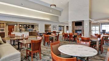 A spacious hotel lobby with multiple seating areas, a fireplace, and a kitchen area.