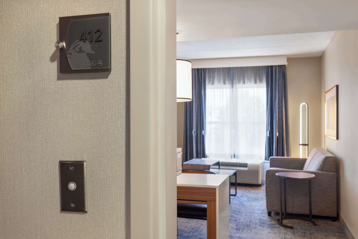 A hotel room with a bed, a desk, a chair, a sofa, a lamp, and a window with curtains.